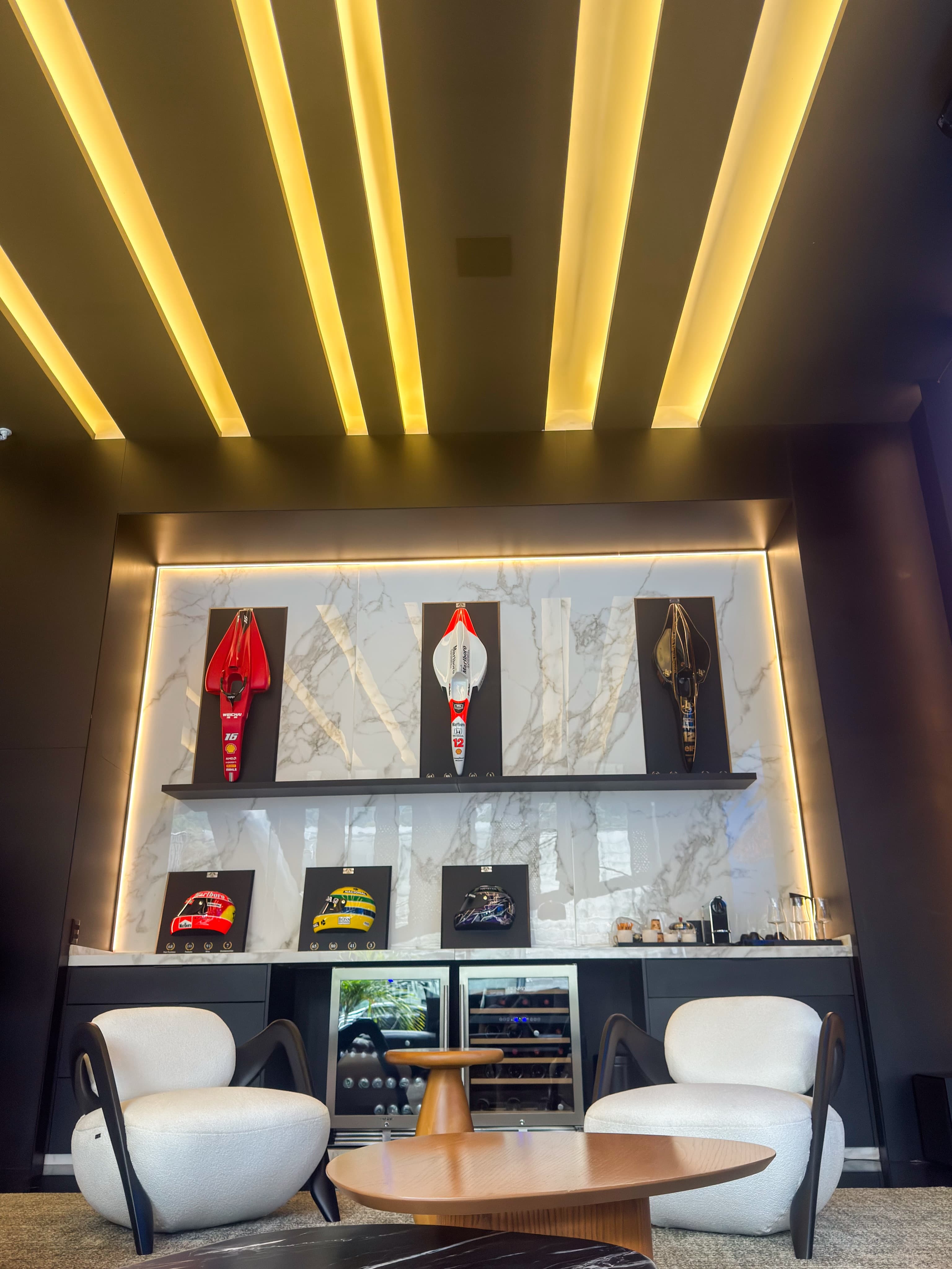 Parede do lounge com capacetes de Fórmula 1 iluminados em nichos de mármore