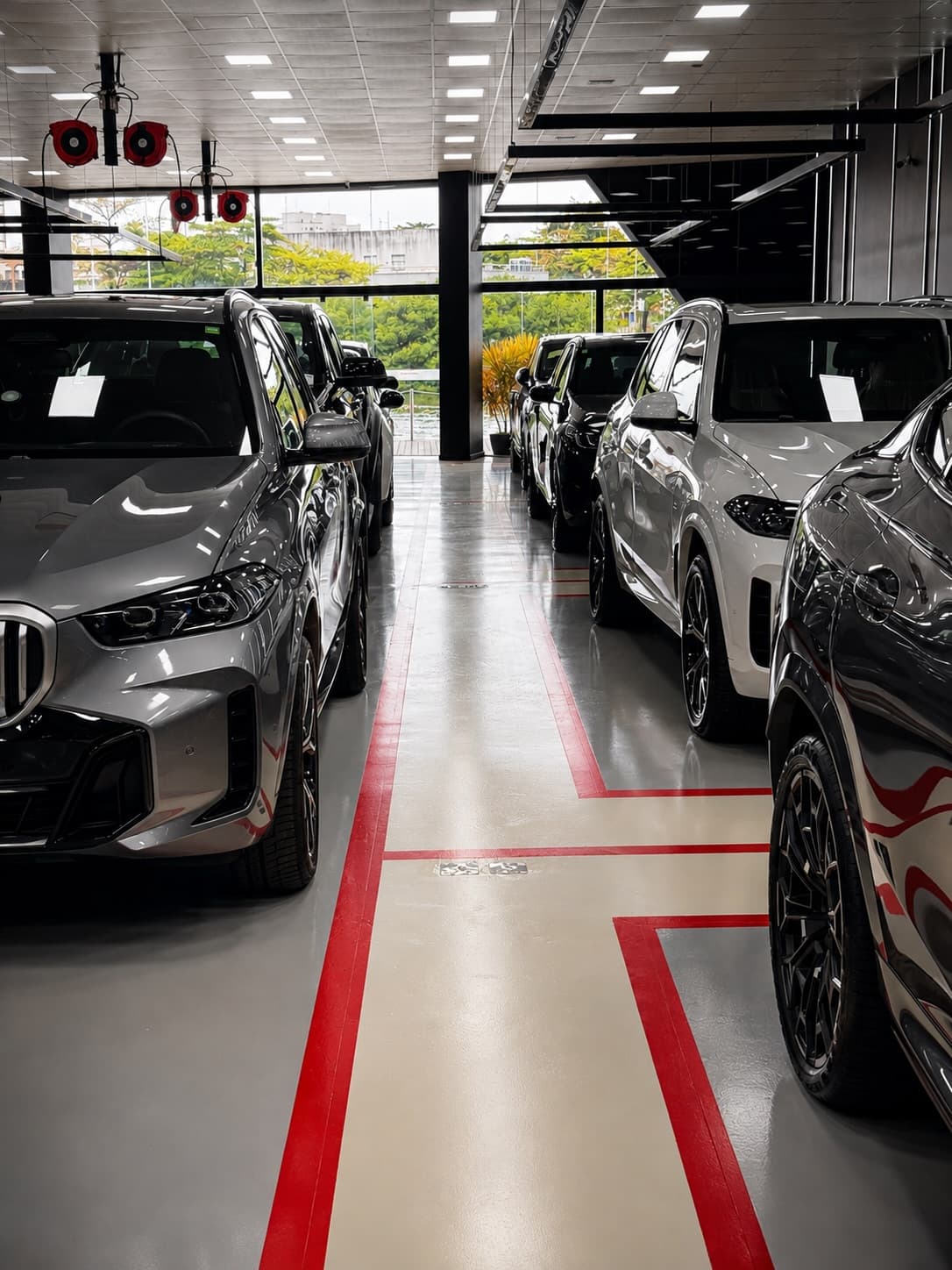 Linha da fábrica com BMW X5 cinza e outros SUVs alinhados sobre o piso com faixas vermelhas