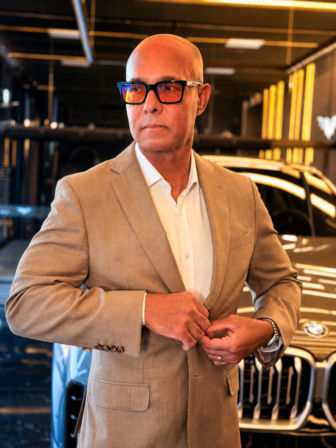 Renato Reis, fundador da Solution Place, de terno bege e óculos, abotoando o paletó diante de uma BMW na Factory Boutique
